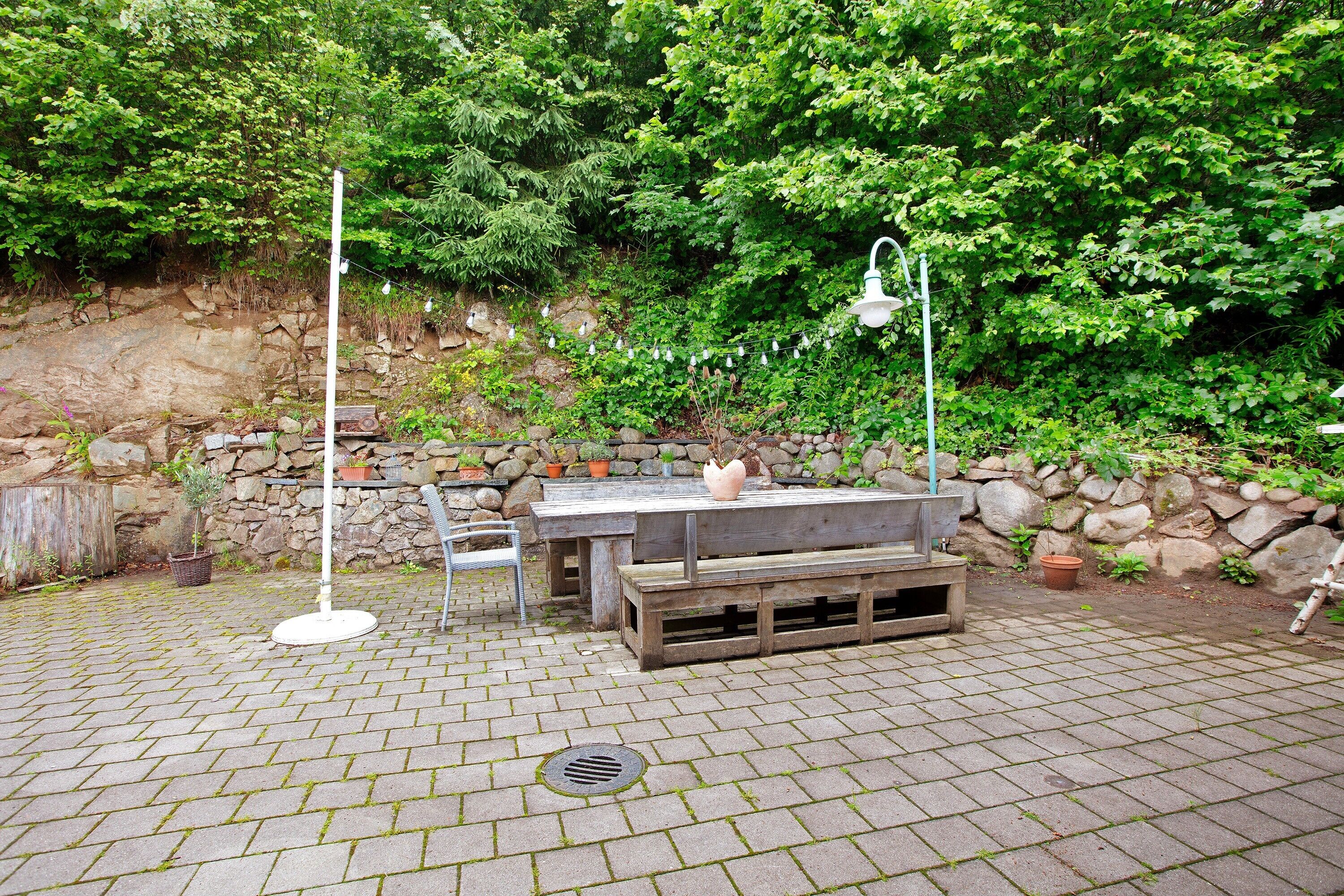 Een terras buiten, met een stenen muur, een houten tafel, banken en lichtjes.