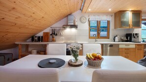 A kitchen with wooden ceiling, white cabinets, a clock, and a window with a view.