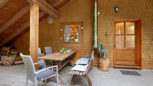 A wooden interior with a dining table, chairs, a bench, a window, and a door.