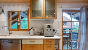 A kitchen with wooden cabinets, a dishwasher, a coffee machine, and a window with a view of a house.