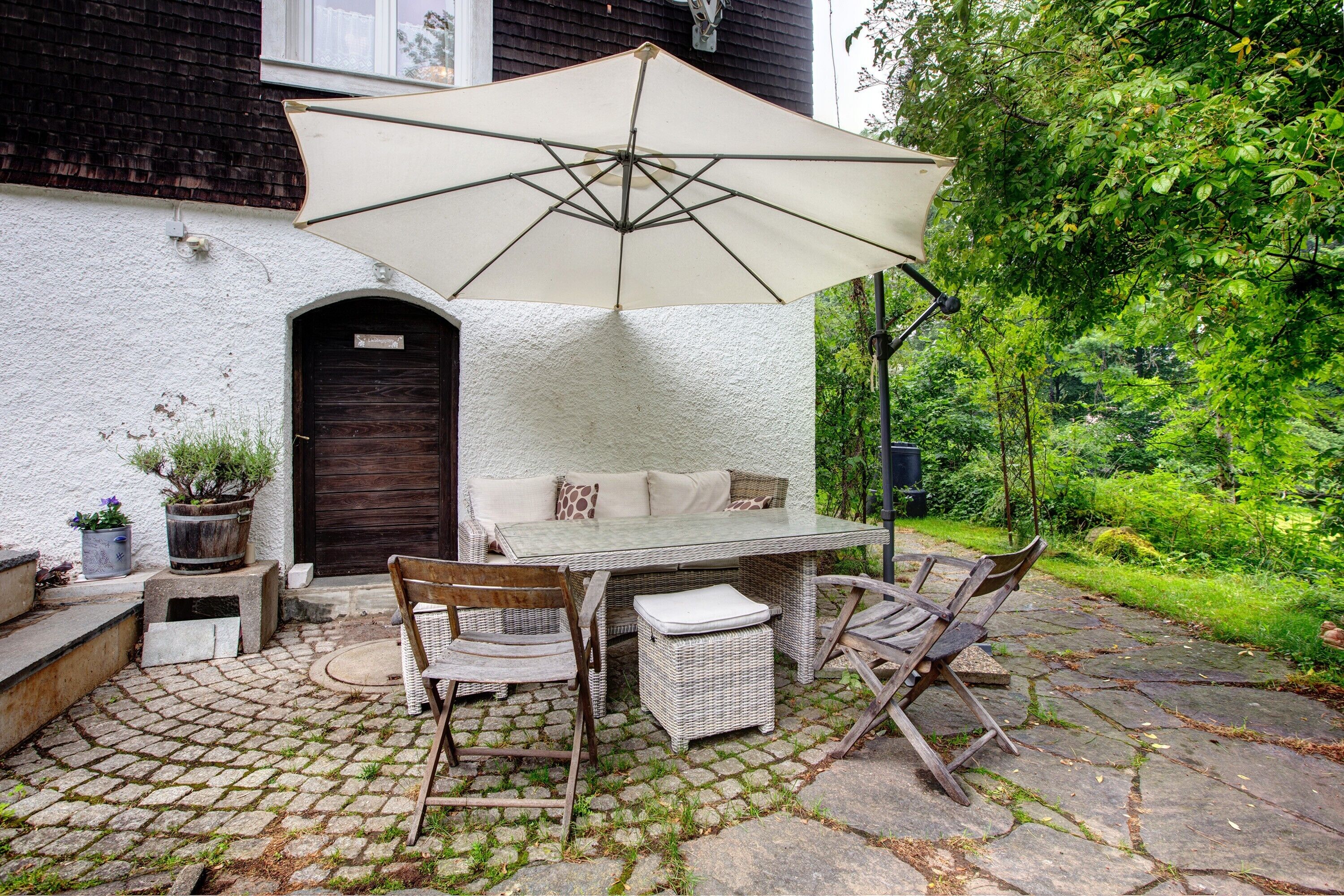 An outdoor patio with a table and chairs, a large umbrella, and a potted plant.