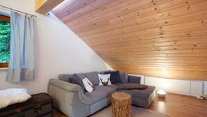 A loft-style room with a grey sectional sofa, a wooden trunk, and a round wooden stool.