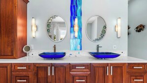A bathroom with two blue vessel sinks, wooden cabinets, and wall-mounted mirrors with decorative lights.