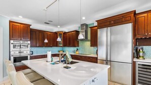 A modern kitchen with wooden cabinets, a stainless steel refrigerator, and a white island with seating.