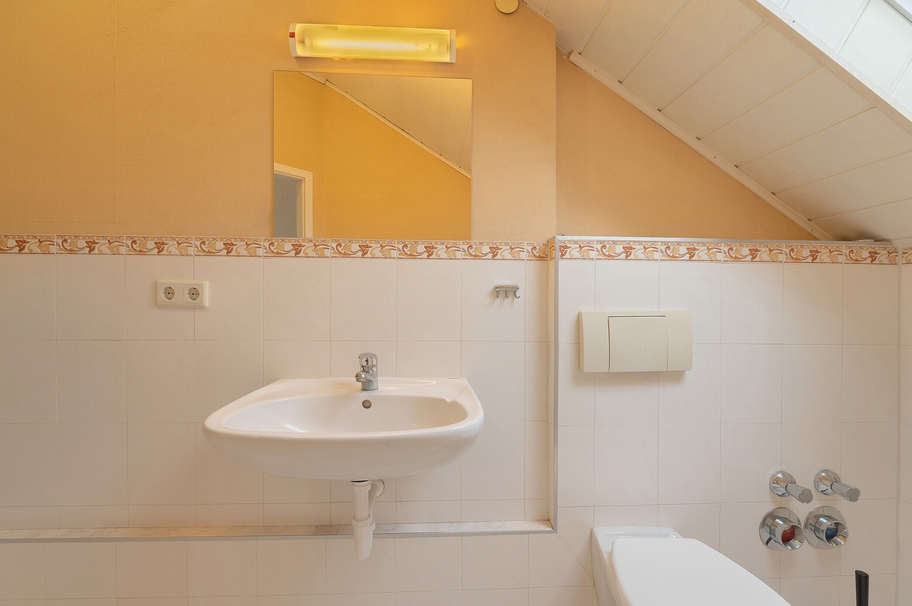 Un baño con lavamanos blanco, un espejo, un perchero y una ducha con panel de control.