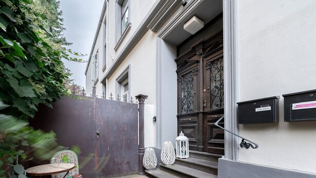 A courtyard with a metal gate, a small round table, a patterned chair, and a white lantern. - Apartment 'Alte Stadtvilla' with Private Garden and Wi-Fi (Neuwied)