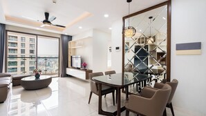 A modern living room with a glass dining table, comfortable seating, a ceiling fan, and a large window offering a city view. - KaLa RiverGate Apartment - Ben Thanh (Ho Chi Minh City)