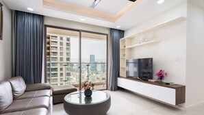 A modern living room with a leather sofa, a glass coffee table, a flat-screen TV, and a city view through large windows. - KaLa RiverGate Apartment - Ben Thanh (Ho Chi Minh City)