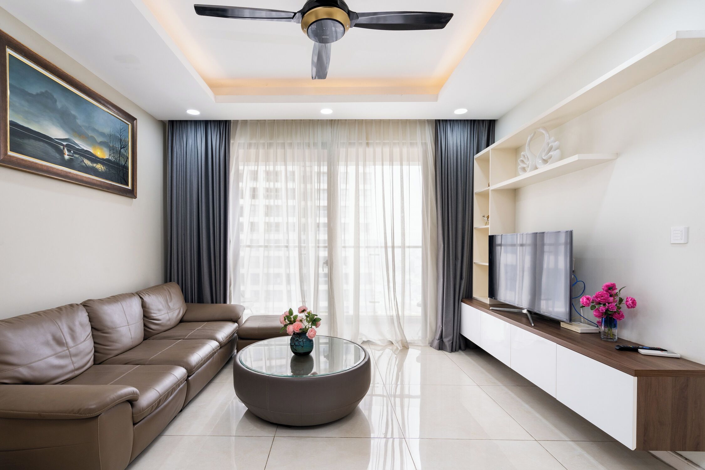 A modern living room with a sofa, a glass coffee table, a TV, and a ceiling fan.