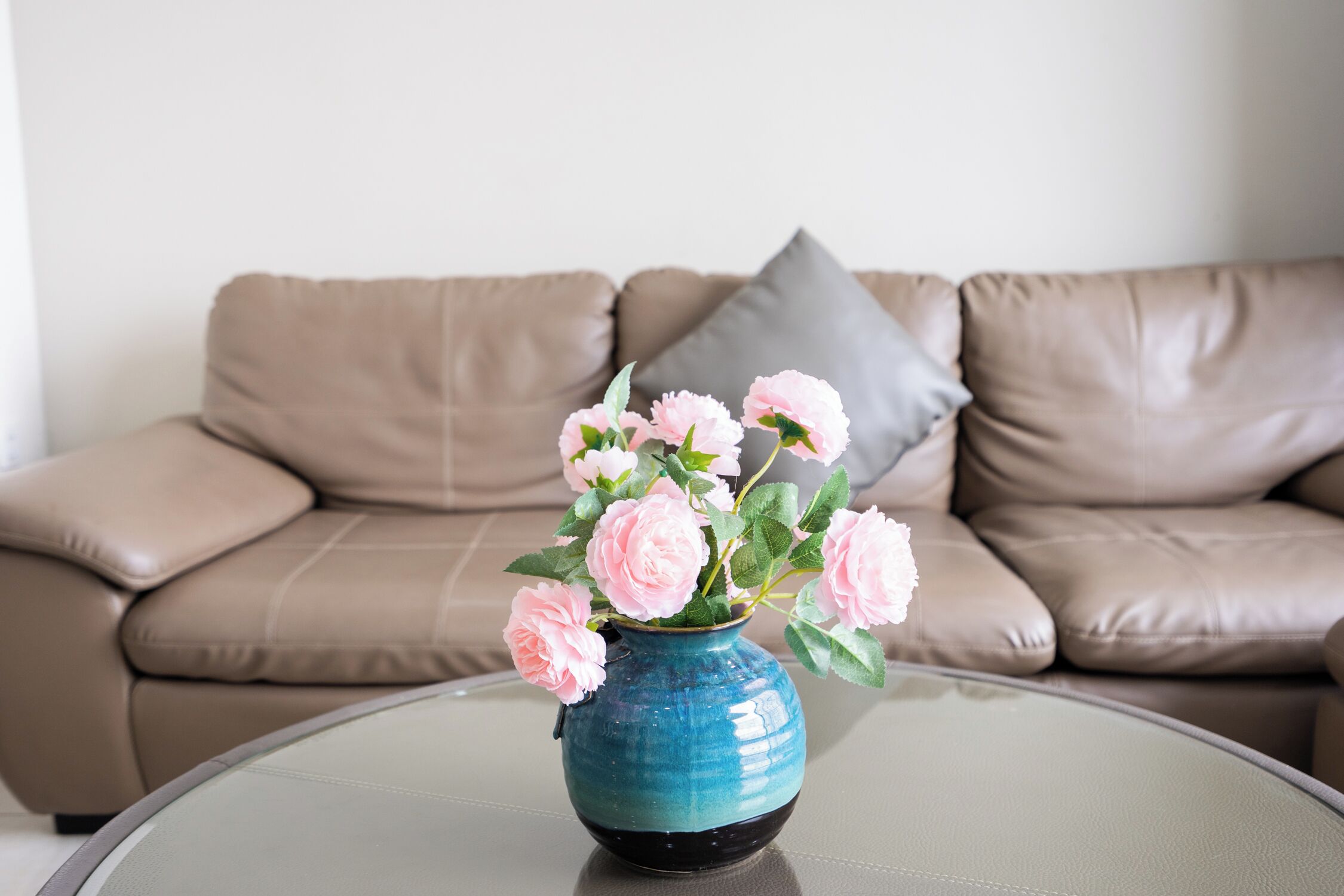 A blue vase with pink flowers on a glass table.