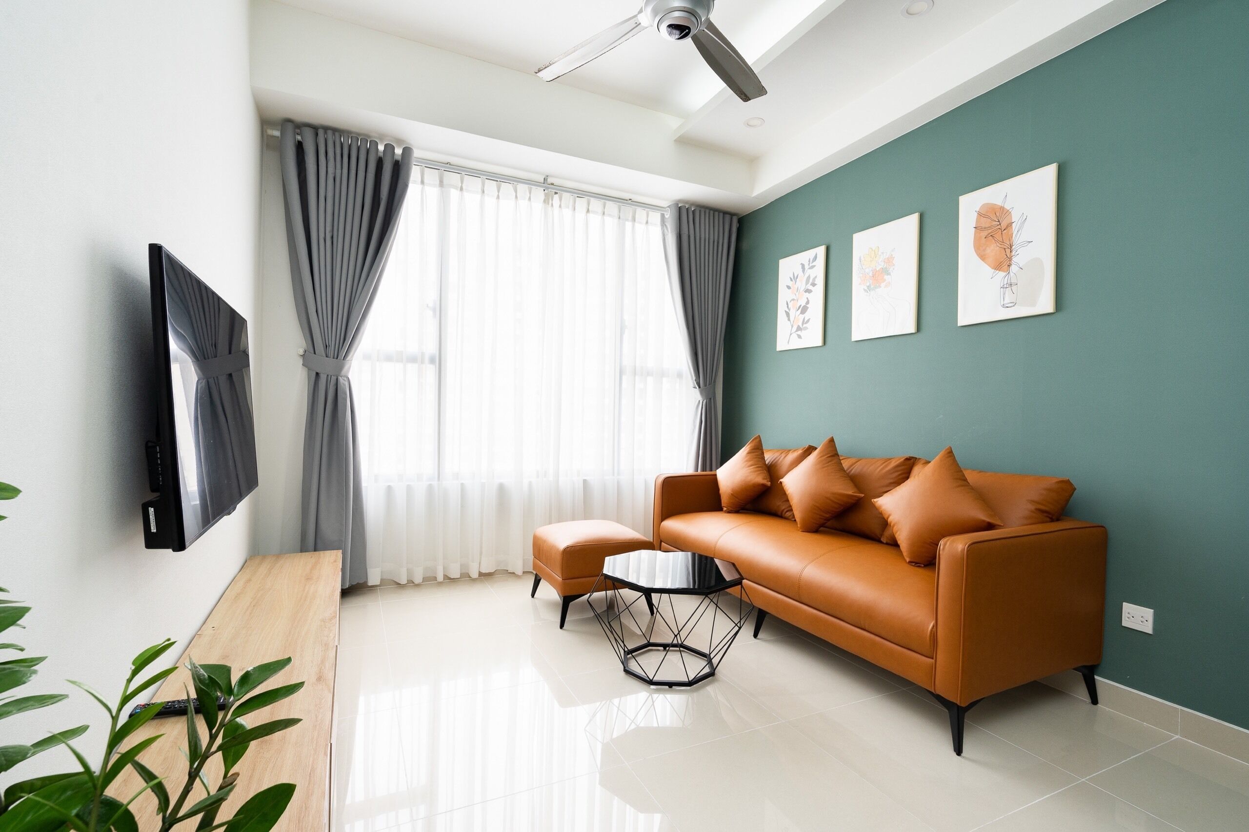 Uma sala de estar moderna com sofá, um banquinho e mesa de centro, televisão de tela plana e obras de arte na parede.