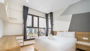 A modern hotel room with a large bed, a wooden desk, and a city view through a large window. - KaLa RiverGate Apartment - Ben Thanh (Ho Chi Minh City)