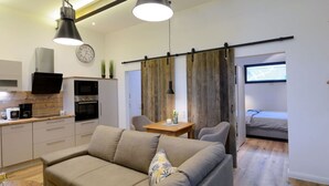 A modern living space with a sofa, dining table, kitchen area, and a sliding door leading to a bedroom. - Deichloft Modern Retreat (Wurster Nordseeküste)