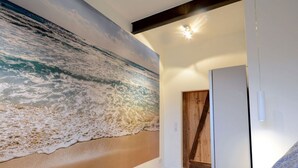 A bedroom with a large ocean mural on the wall, a bed with patterned pillows, and a wooden door. - Deichloft Modern Retreat (Wurster Nordseeküste)
