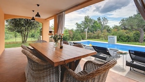 Un espace extérieur abrité, aménagé pour les repas, avec vue sur la piscine, du mobilier en osier et une table en bois.