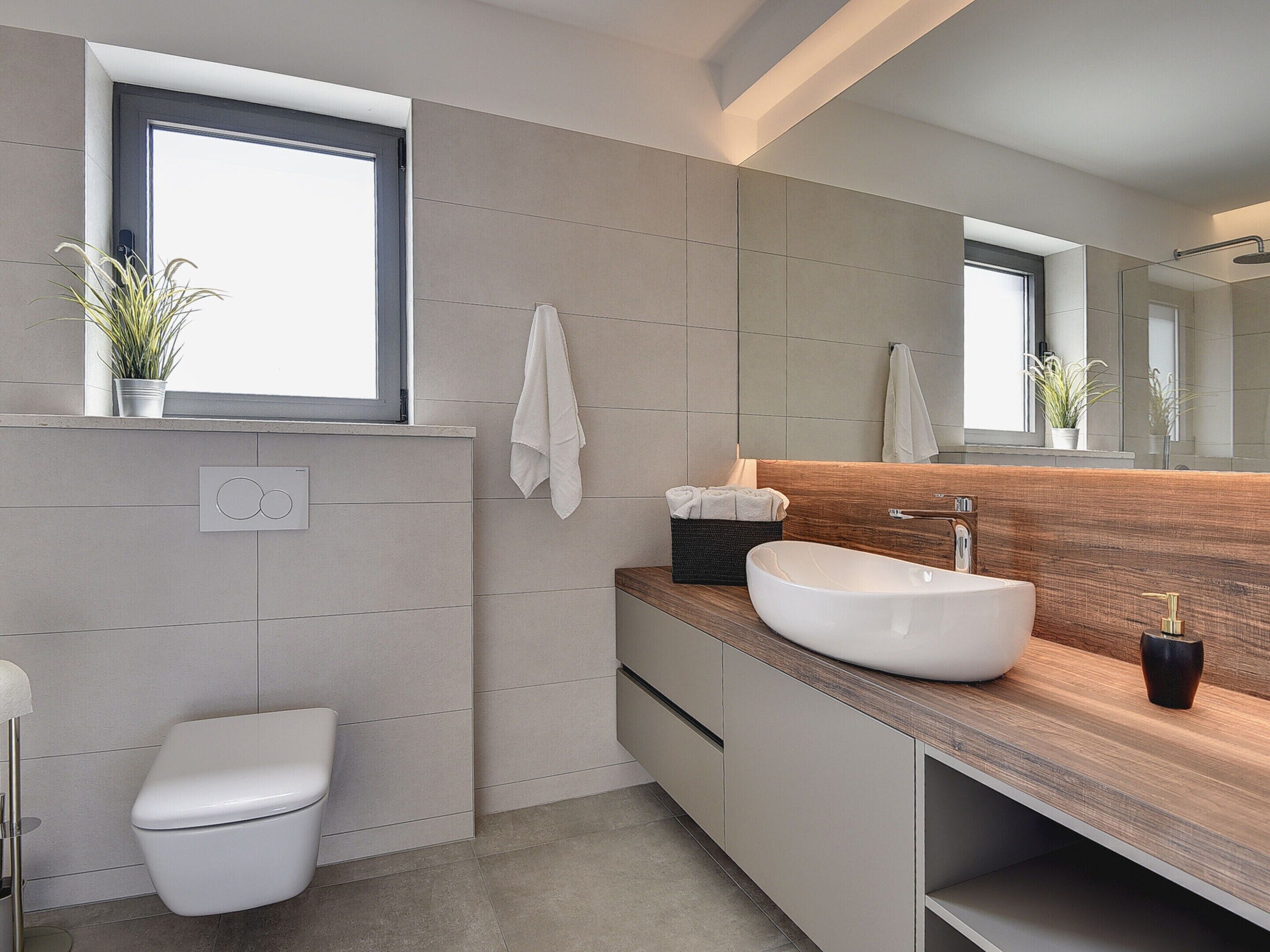 Une salle de bain moderne avec un grand miroir, un meuble-lavabo en bois, un lavabo blanc et des toilettes.