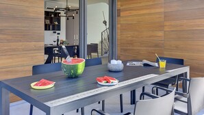 Un espace repas moderne avec une longue table, des chaises et une grande pastèque servant de centre de table.