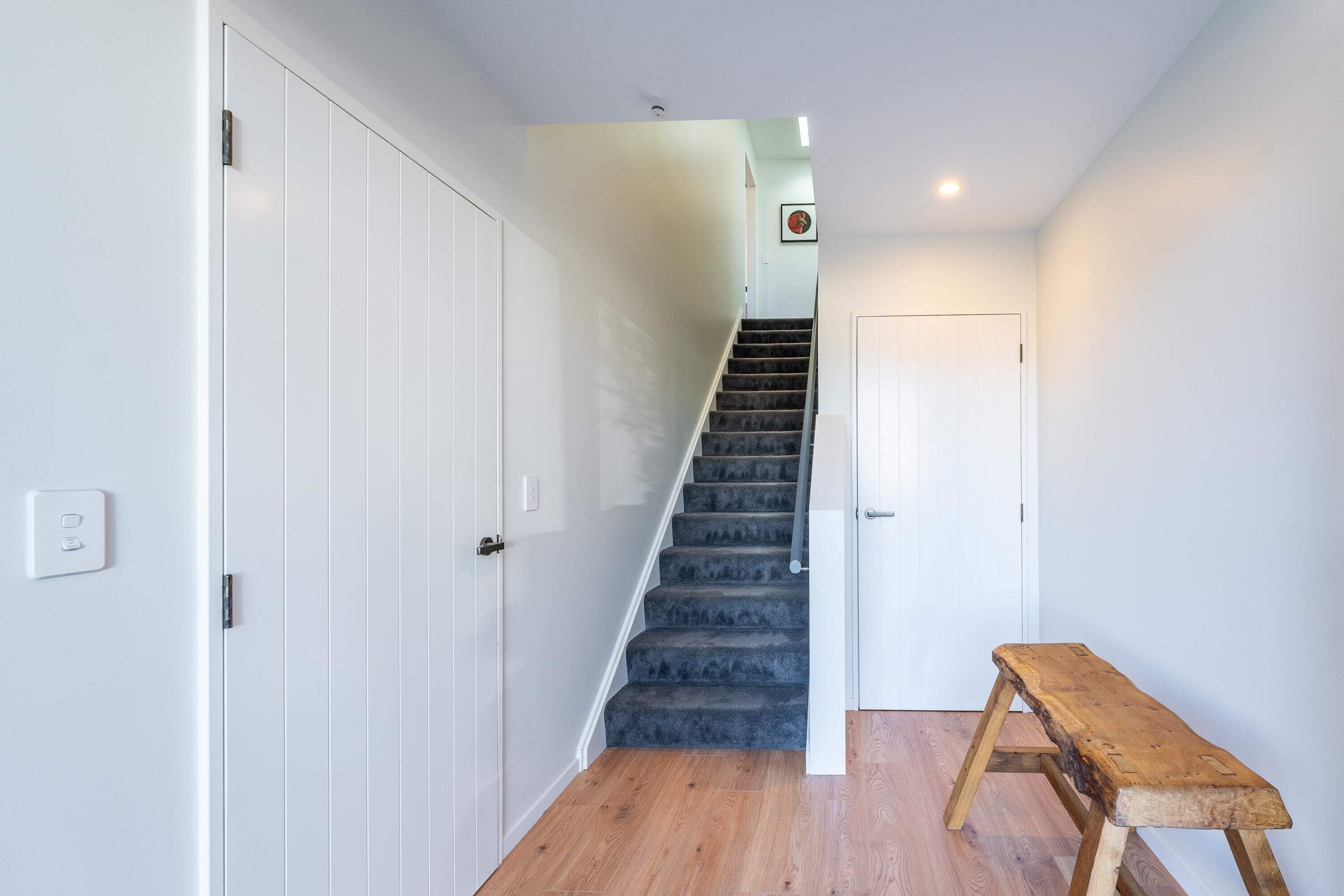 A staircase leading to a door, a wooden bench, and a light switch on the wall.