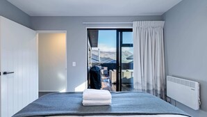 A modern hotel room with a large bed, a view of the mountains through the window, and a sliding door leading to an outdoor area. - Cosy Kirimoko Escape in Wanaka (Wānaka)