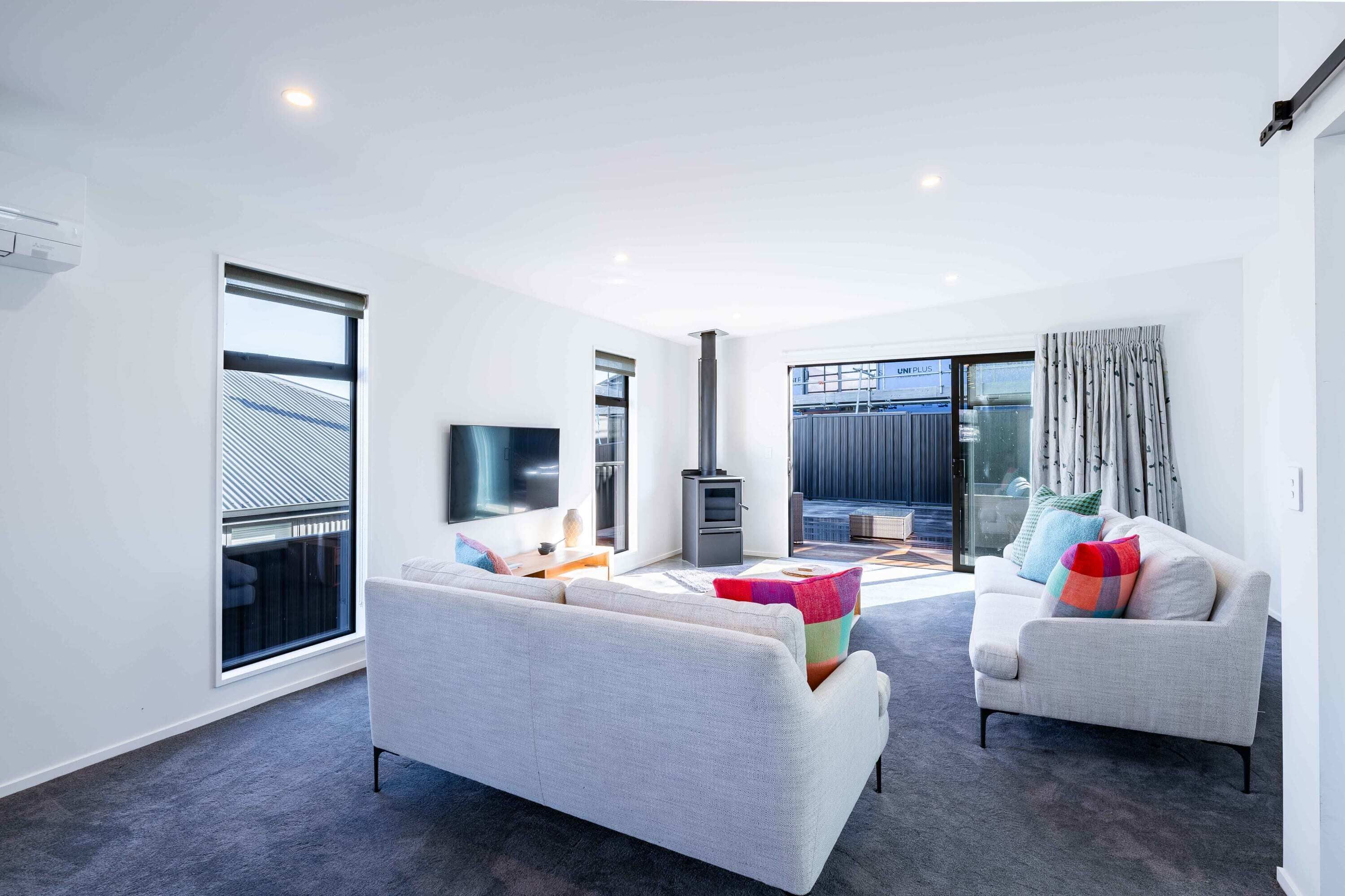 A modern living room with a sofa, a coffee table, and a TV. There is a large window and a fireplace.