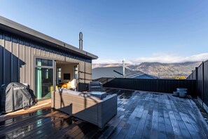 A rooftop patio with a wicker sofa, a grill, and a view of mountains. - Cosy Kirimoko Escape in Wanaka (Wānaka)