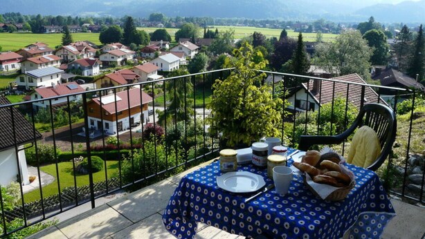 Balcón con mesa lista para el desayuno, con vistas a una zona residencial y montañas.