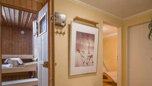 Una habitación con techo de madera, sauna, un cuadro enmarcado en la pared y una pequeña mesa con objetos rosados.