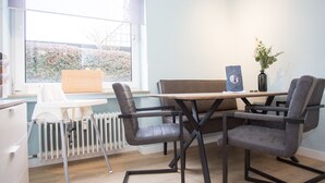 A modern room with a dining table, two chairs, a radiator, and a window with a view of greenery.