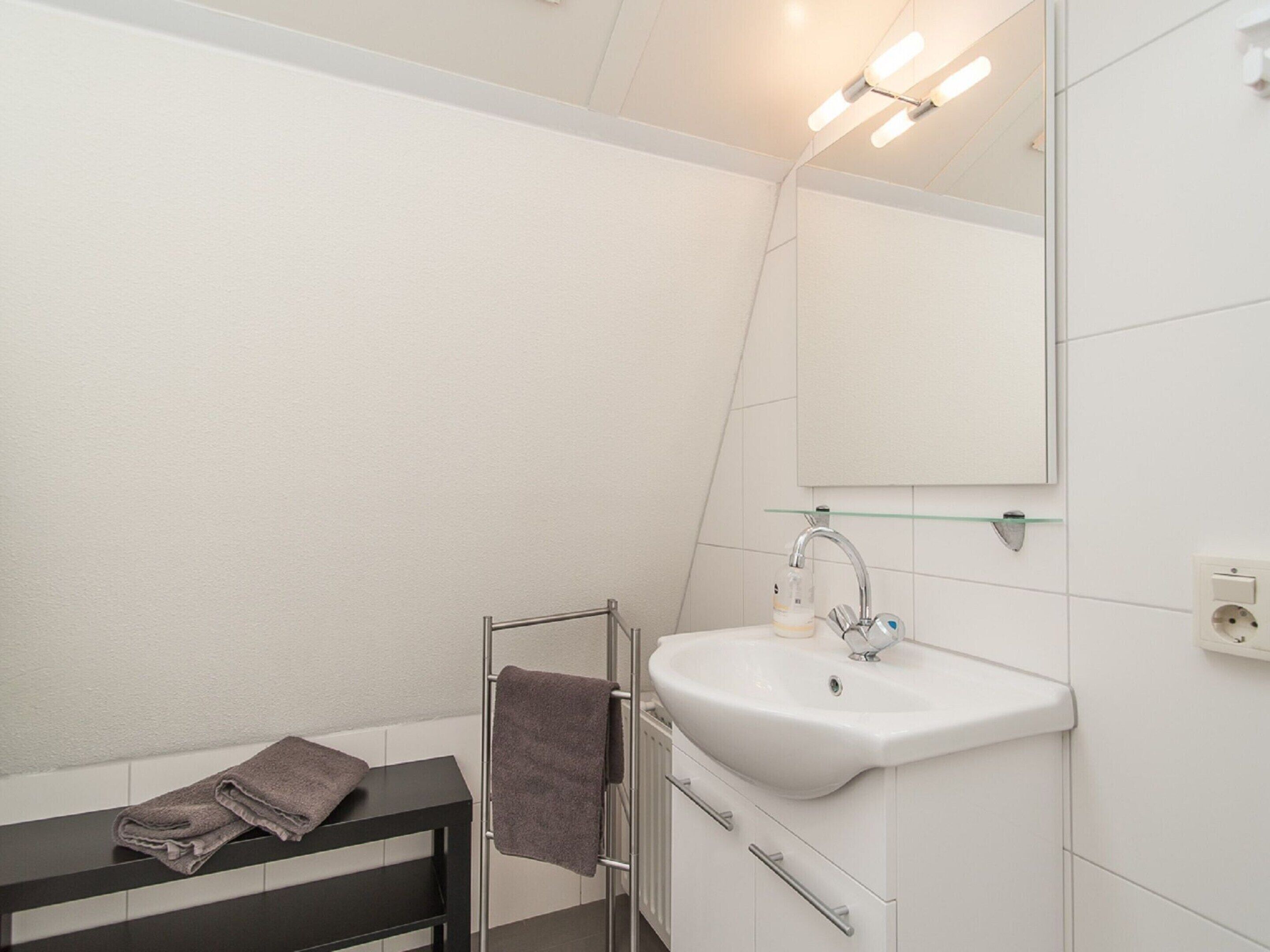 Un baño moderno con un lavamanos blanco, un estante de vidrio sobre el lavamanos, un perchero con una toalla y un espejo.
