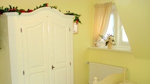 A bedroom with a white wardrobe, a small window with curtains, a radiator, and a floral bedspread. - Holiday Apartment Bella Rosa Luneburg (Reppenstedt)