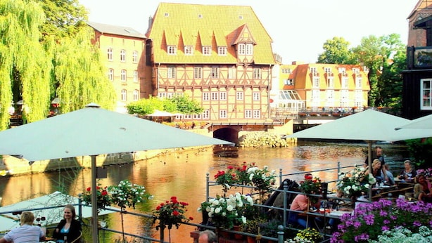 A riverside dining area with outdoor seating, a bridge, and traditional buildings in the background. - Holiday Apartment Bella Rosa Luneburg (Reppenstedt)