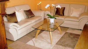 A living room with a beige sofa, a glass coffee table, and a small potted plant. - Holiday Apartment Bella Rosa Luneburg (Reppenstedt)