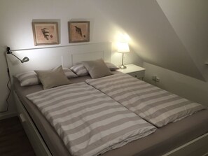 A single-bed room with a sloped ceiling, a bedside table with a lamp, and two framed pictures on the wall.
