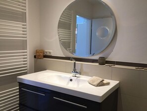 A bathroom with a white sink, a round mirror, and a towel on the counter.