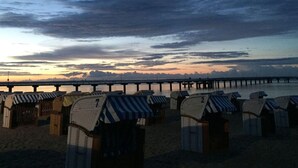 Des cabanes de plage avec des auvents rayés, une jetée en arrière-plan et un ciel au coucher du soleil.