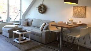 Un salon moderne avec un canapé gris, des chaises blanches, une table en bois et un luminaire suspendu.