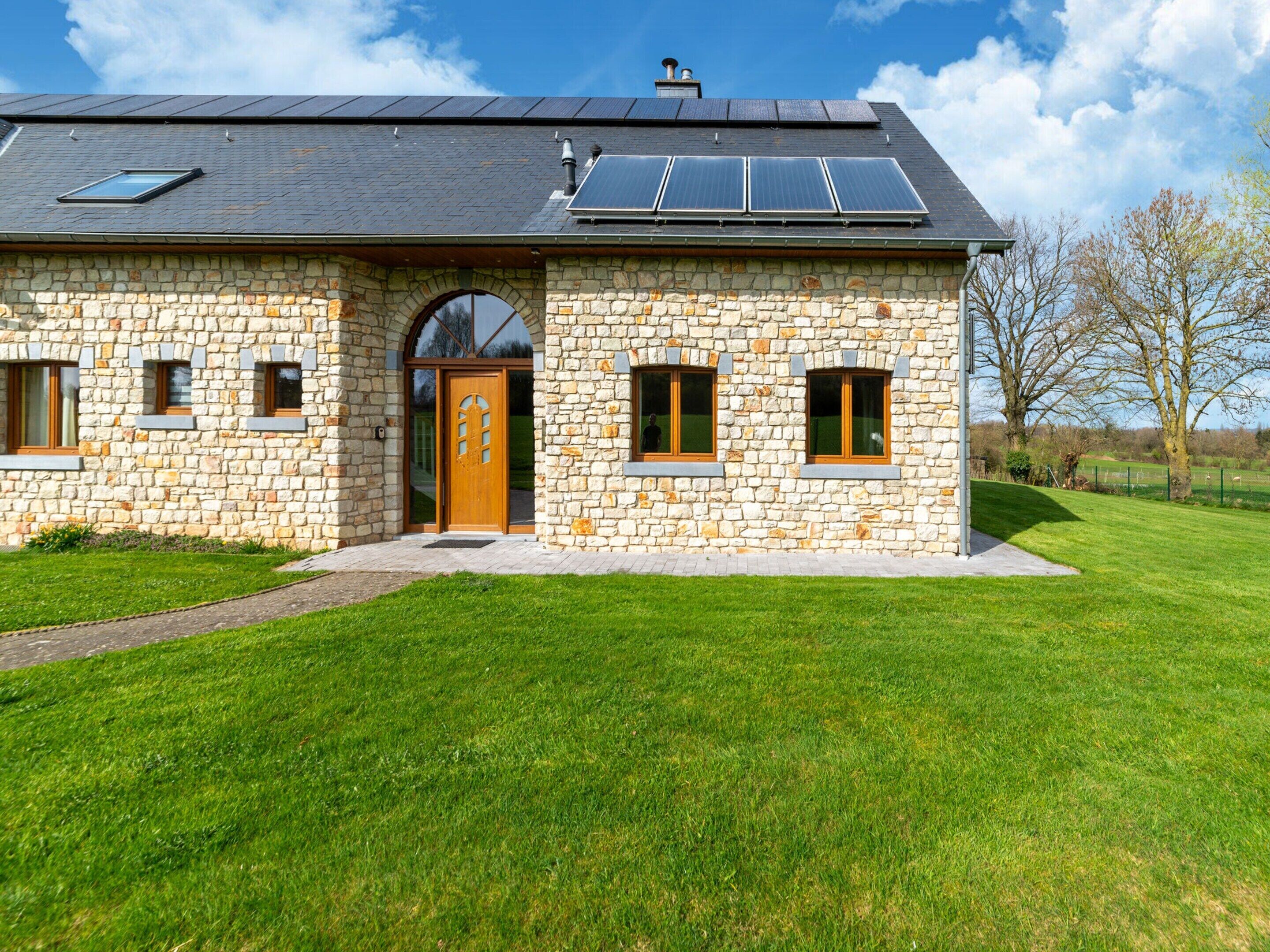 A stone house with a large wooden door, solar panels, and a grassy yard.