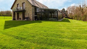 Une maison en pierre avec une véranda en verre, une pelouse et un ciel dégagé.