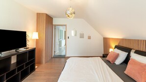Une chambre moderne avec un grand lit, un téléviseur posé sur un meuble et un dressing.