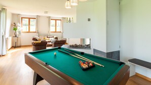 Une table de billard dans une pièce avec un canapé, une cheminée et de grandes fenêtres.