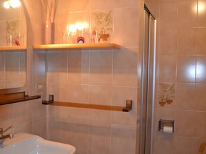 A bathroom with a white sink, a mirror, and a shower area. There are shelves with toiletries and a towel rack. - Pet-friendly Mountain Home (Cavalese)