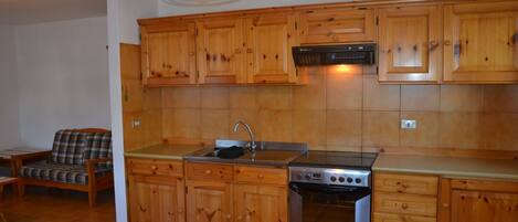 Cocina con armarios de madera, estufa de acero inoxidable y una lámpara colgante roja.