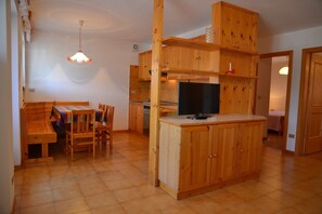 A compact kitchen with wooden cabinets, a dining area with a bench and chairs, and a small island with a sink. - Pet-friendly Mountain Home (Cavalese)