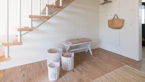 A staircase with wooden steps and white railings, a bench with cushions, and wicker baskets on the floor. - Holiday Home Meerperle (Butjadingen)