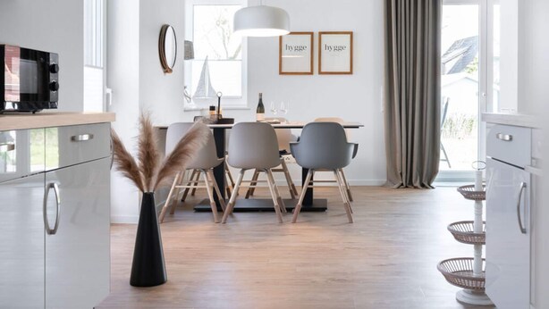 A modern kitchen with a dining area, featuring a microwave, a dining table with chairs, a hanging light fixture, and framed artwork on the wall. - Holiday Home Meerperle (Butjadingen)