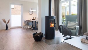 A modern living room with a wood-burning stove, a dining area, and a view of the outdoors. - Holiday Home Meerperle (Butjadingen)