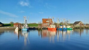 A calm harbor with several fishing boats docked, a red building, and a green field in the background. - Holiday Home Meerperle (Butjadingen)