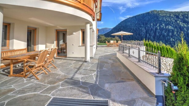 A hotel with a stone patio, wooden furniture, and a view of a forested mountain.