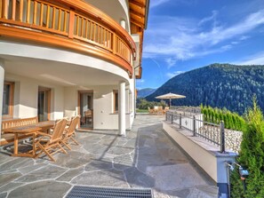 A hotel with a stone patio, wooden furniture, and a view of a forested mountain. - Neunerspitze Comfortable Holiday Residence (San Lorenzo di Sebato)