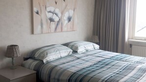 A bedroom with a bed, two bedside tables, and a window with curtains. - Helmduin 5D Comfortable Holiday Residence (Egmond aan Zee)